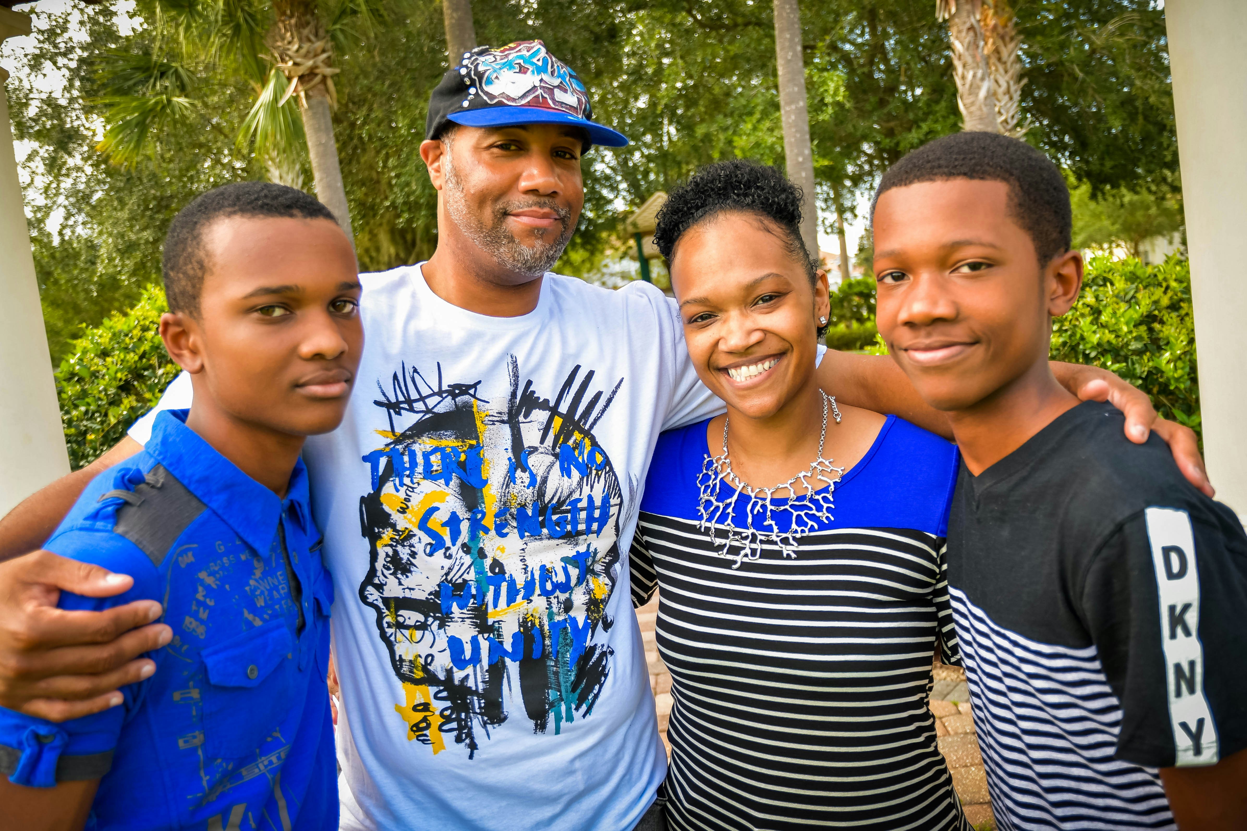 A father, mother and two teenage sons standing arm in arm outdoors, smiling